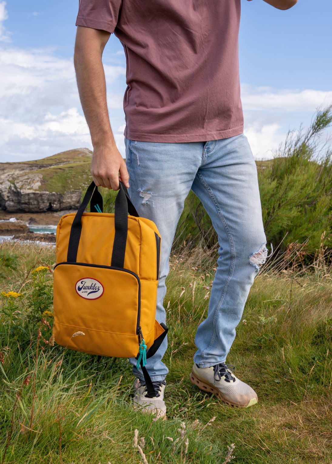 Person holding a yellow backpack outdoors with a scenic background