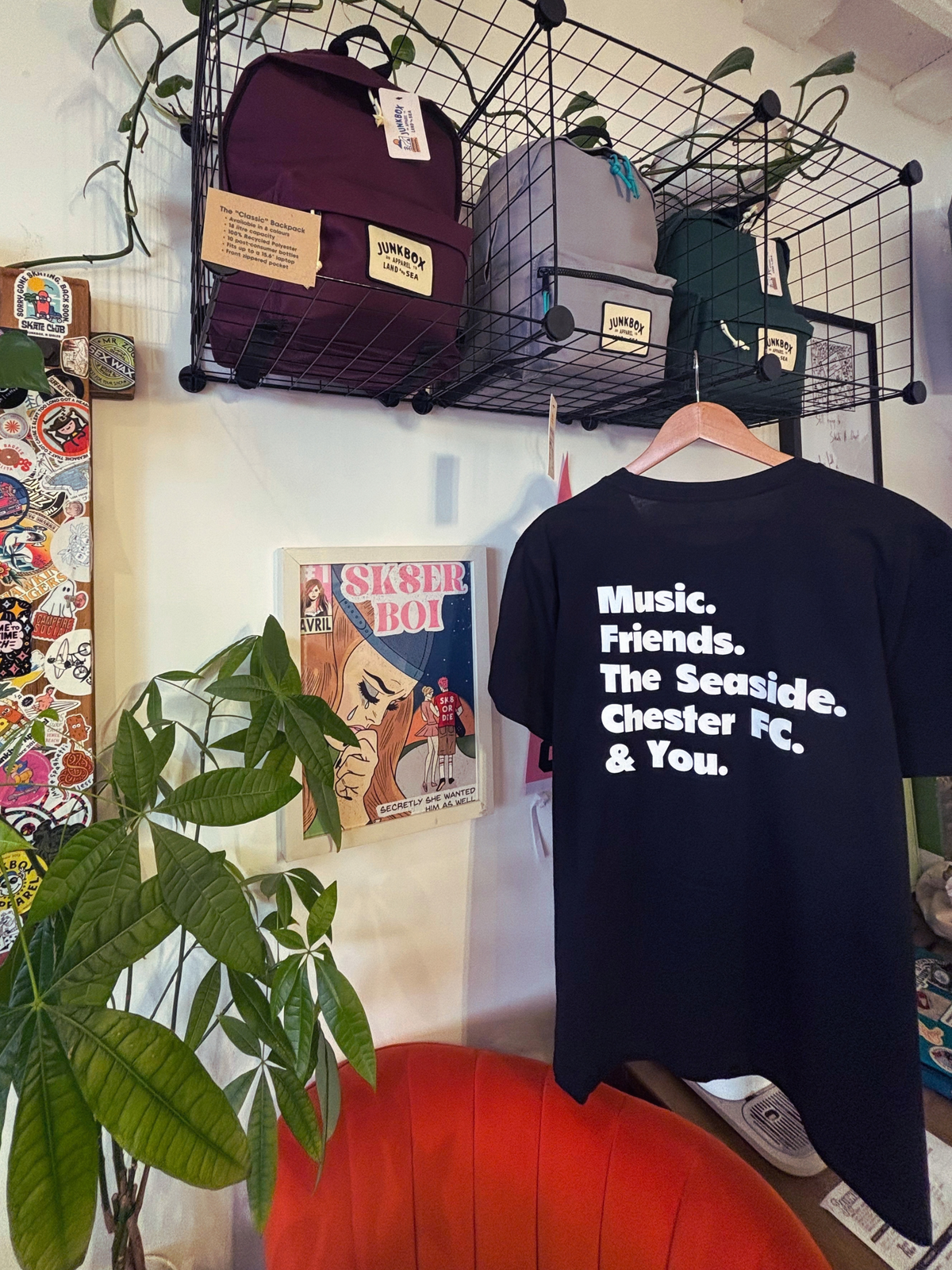 A black graphic t-shirt hanging on a wooden hanger against a white wall, featuring the text 'Music. Friends.
