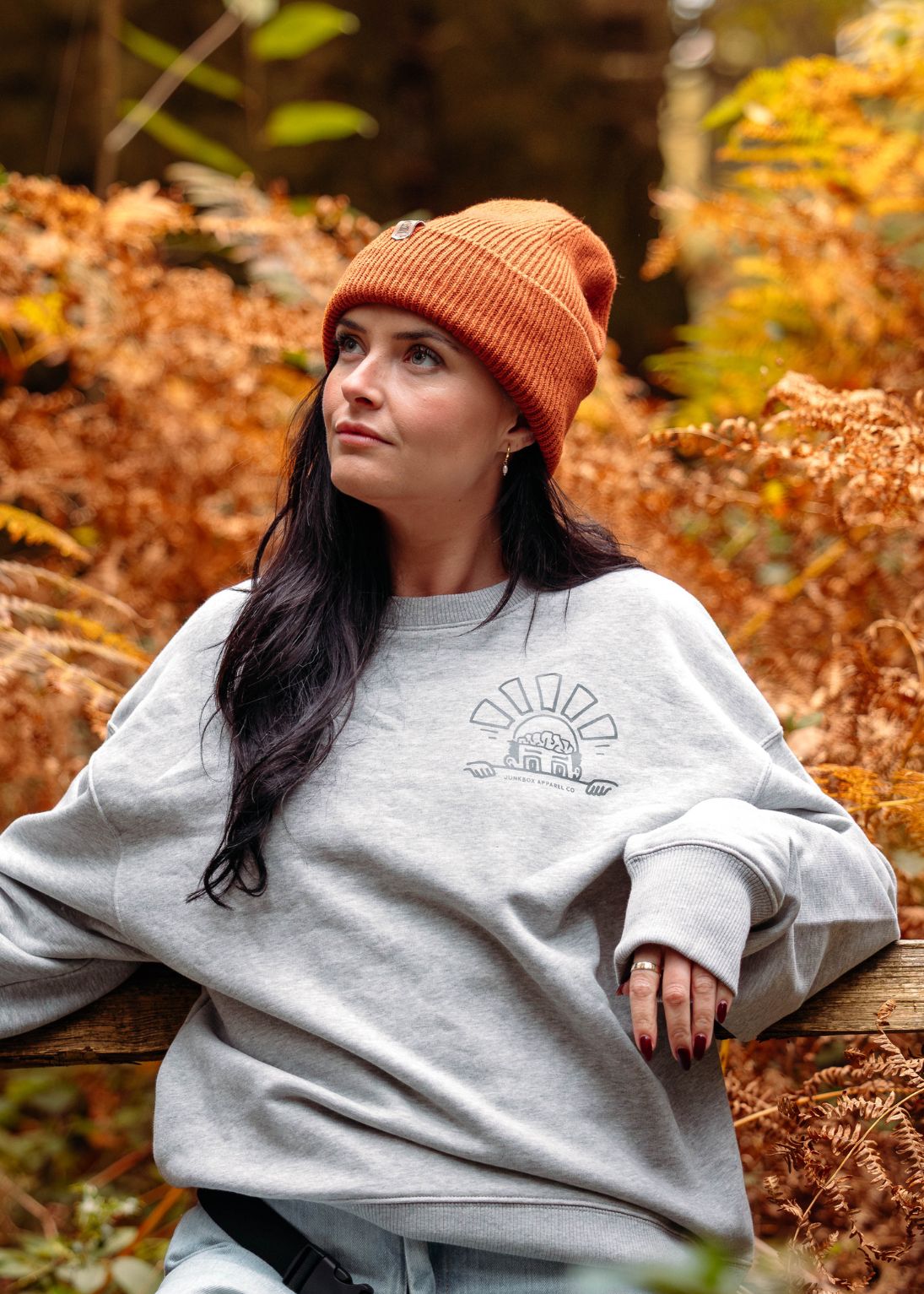 Woman wearing a gray sweatshirt with a design, sitting in an autumn forest.