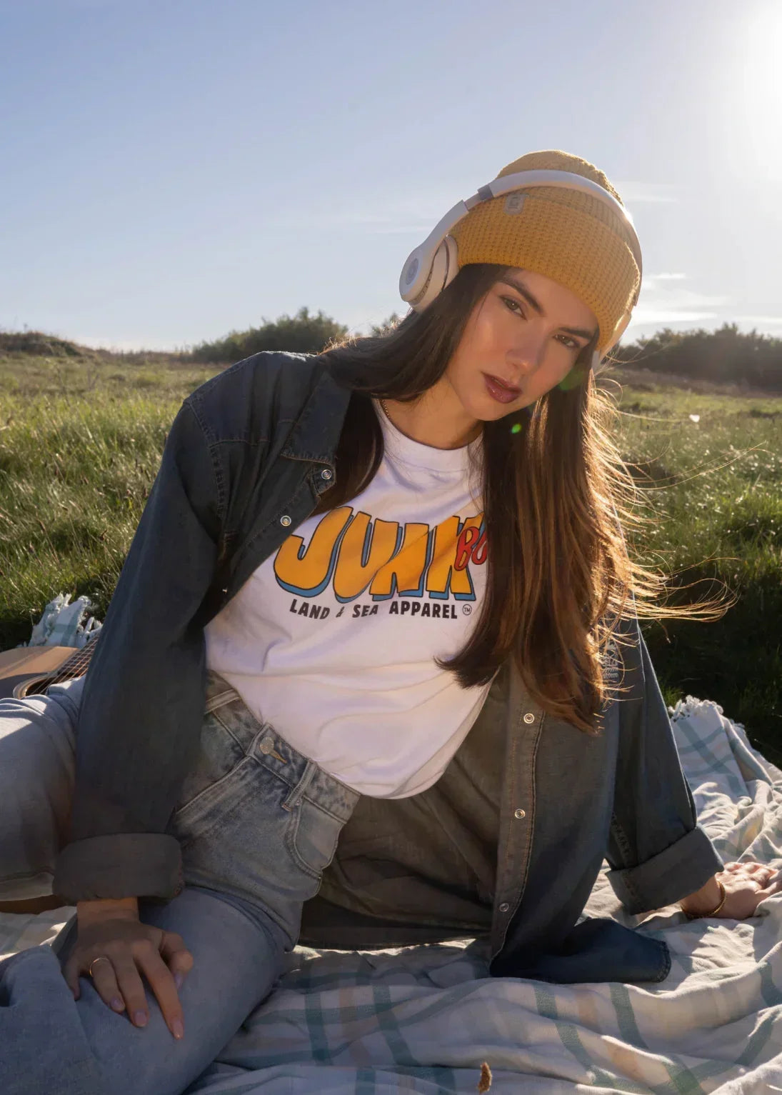 Woman outdoors in yellow beanie and headphones, wearing eco-friendly graphic t-shirt and denim