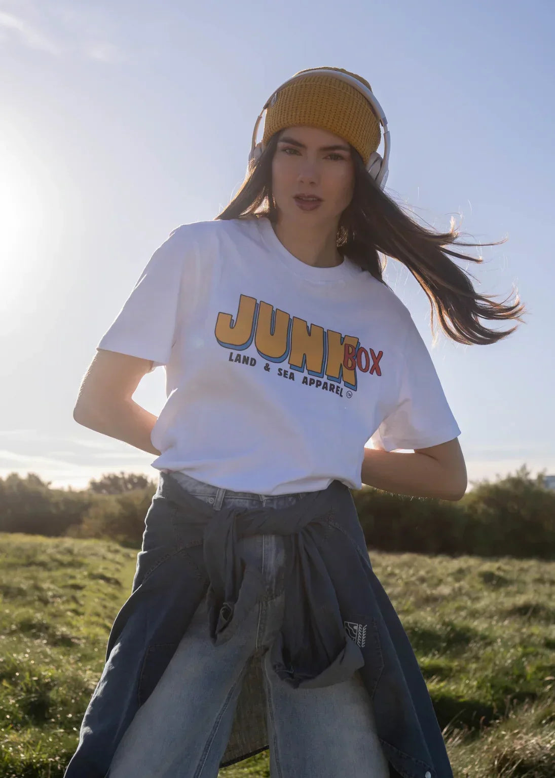 Woman outdoors in casual eco-friendly t-shirt, yellow beanie, and headphones, daytime