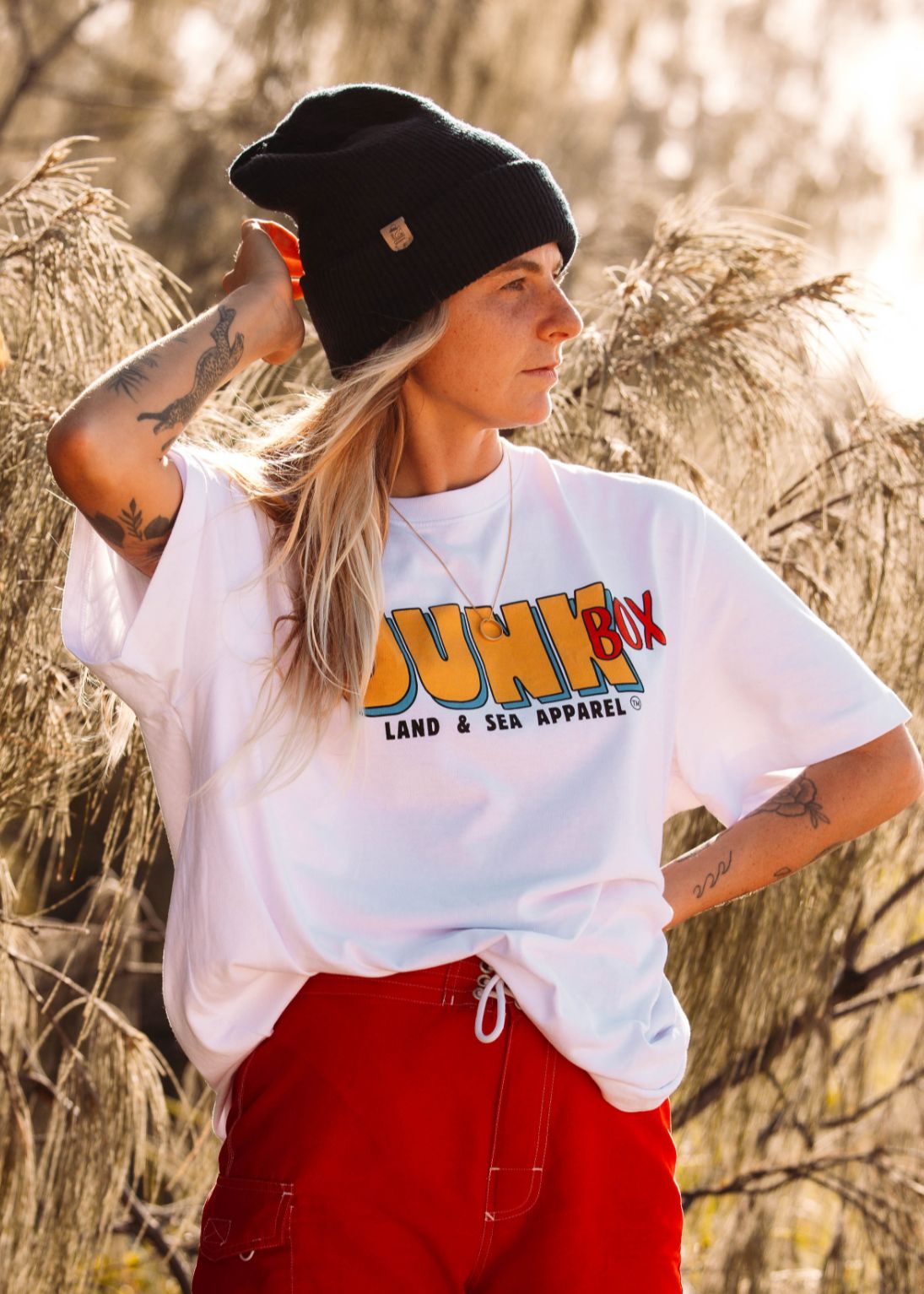 Person wearing a white t-shirt with 'Junk' branding, black beanie, and red pants standing outdoors.