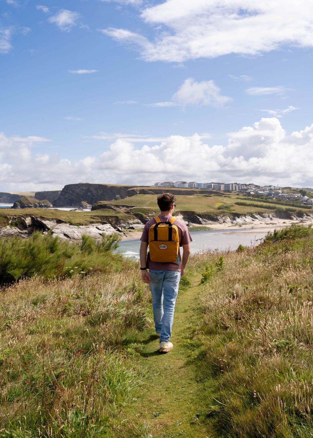 Person with a yellow backpack walking along a coastal path with a scenic view.