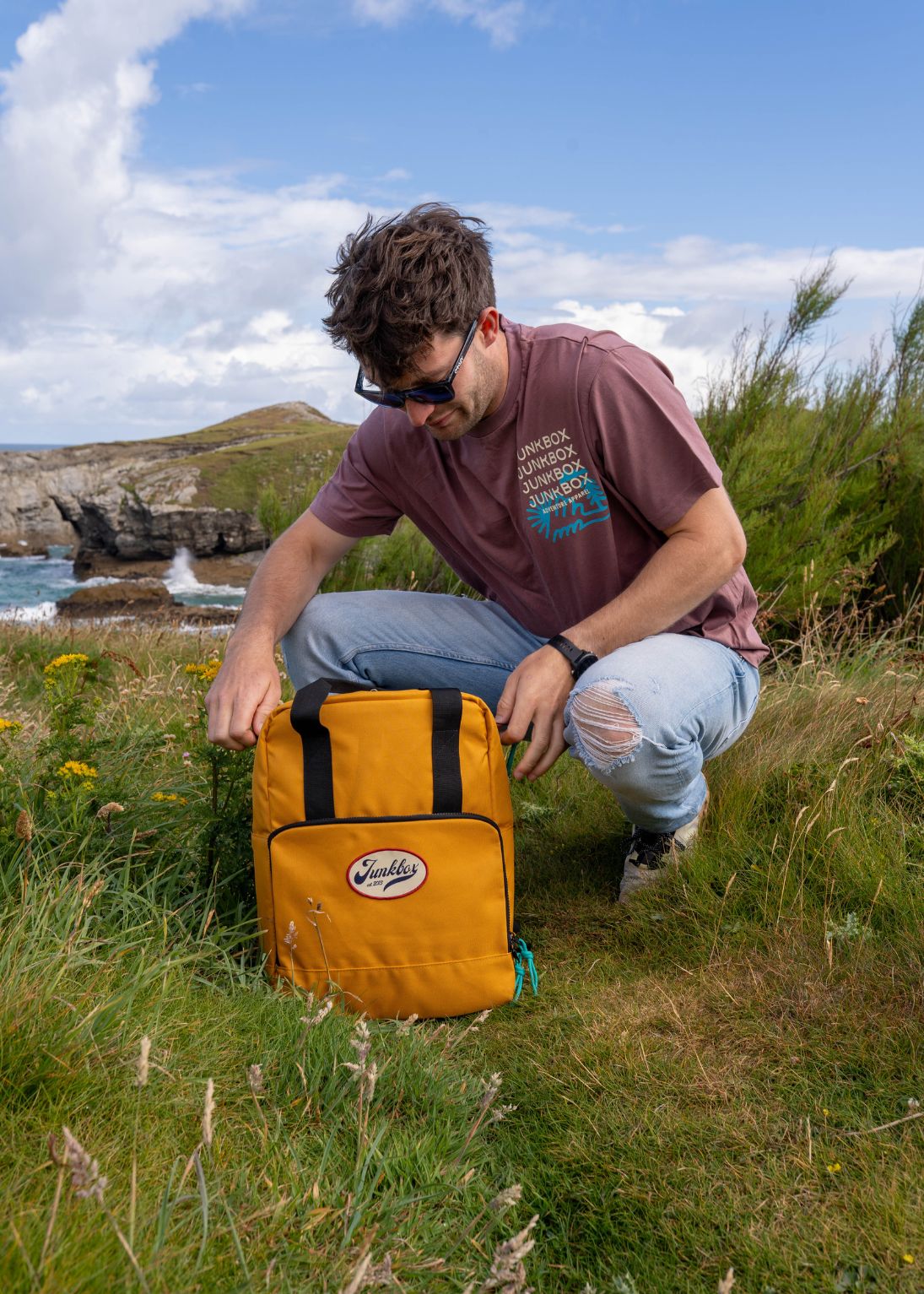 Person kneeling in a grassy outdoor area with a yellow backpack