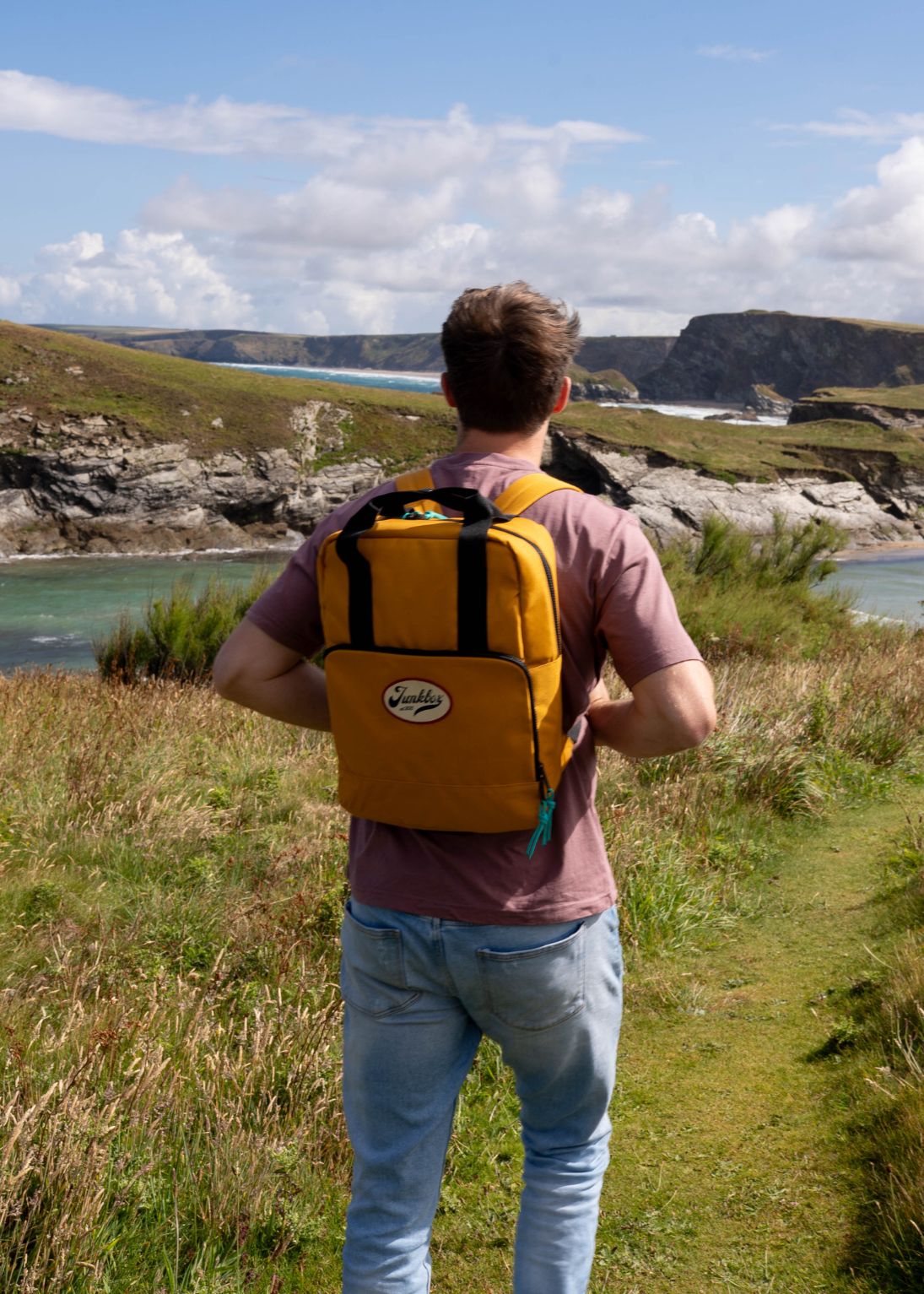 Person with a yellow backpack standing on a grassy hill overlooking a scenic landscape.