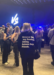 Person wearing a black sweatshirt with text at an event with 'VS' branding.