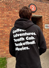 Person wearing a black hoodie with text on the back in front of a brick wall.