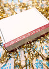 Decorative box with a red and white design on a festive background with gold tinsel and blue ribbons.
