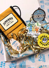 Collection of Junkbox branded items including a yellow bag, stickers, and a sex wax air freshener on a patterned surface.