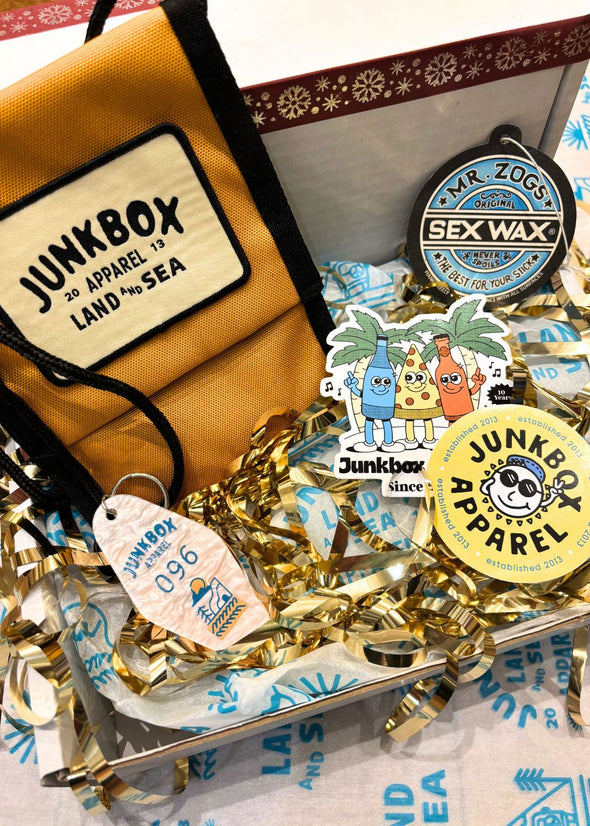 Junkbox Apparel branded items including a bag, stickers, and a sex wax air freshener on a decorative background.