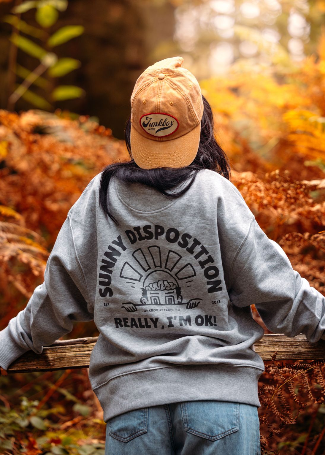 Person wearing a gray sweatshirt with text and a cap in an autumn setting